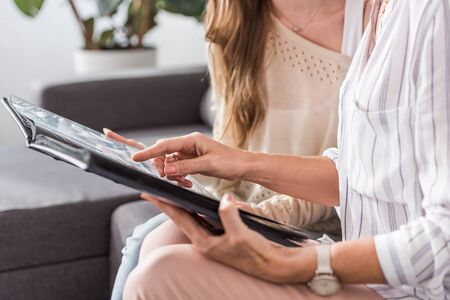 cropped view of woman pointing with finger at photo album while sitting near daughterの写真素材