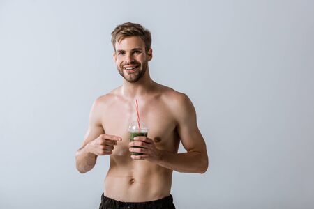 front view of smiling shirtless sportsman pointing with finger at smoothie isolated on greyの写真素材
