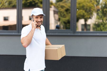 happy delivery man talking on smartphone while holding boxの写真素材
