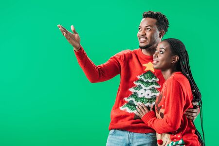 African American man pointing with hand near woman in Christmas sweater isolated on greenの写真素材