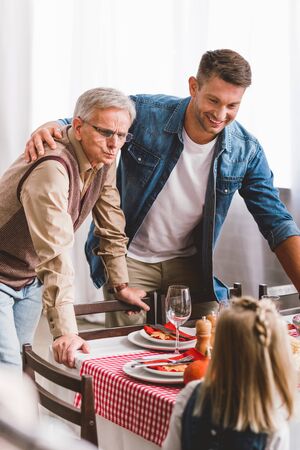 selective focus of smiling father and grandparent looking at kid in Thanksgiving dayの写真素材