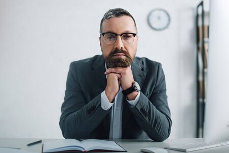 handsome businessman in formal wear and glasses looking at camera in officeの写真素材