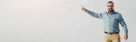 panoramic shot of handsome and smiling businessman in shirt pointing with fingerの写真素材