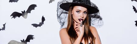 panoramic shot of girl in black witch Halloween costume near white wall with decorative batsの写真素材