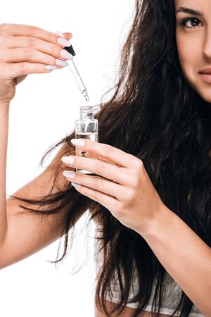 cropped view of brunette beautiful woman with damaged hair holding oil isolated on white