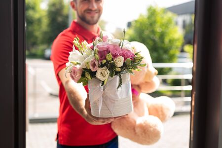 cropped view of bearded delivery man holding teddy bear and flowersの写真素材