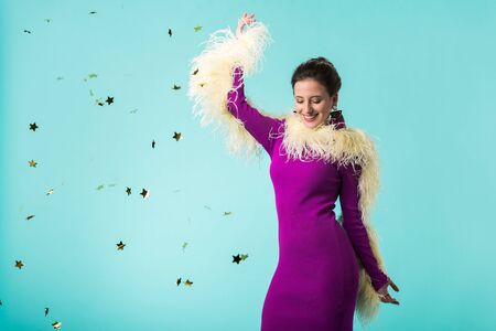 happy party girl in purple dress with feathers dancing under falling confetti isolated on turquoise