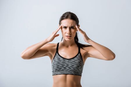 attractive sportswoman with headache touching temples isolated on grey