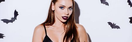 panoramic shot of girl in black dress near white wall with decorative batsの写真素材