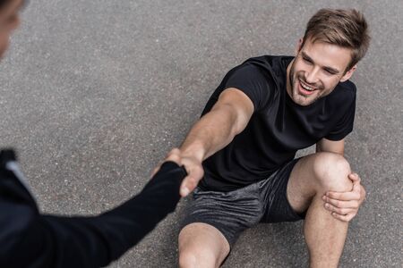 cropped view of woman helping sportsman with injured knee on street
