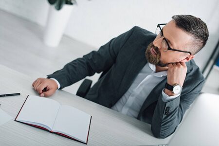 handsome businessman in formal wear and glasses looking away in office の写真素材