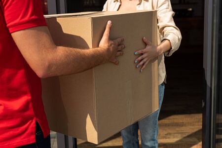 cropped view of delivery man giving carton box to woman