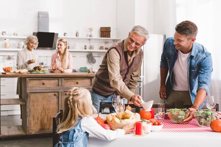 selective focus of smiling father and grandparent looking at kid and setting table in Thanksgiving dayの写真素材