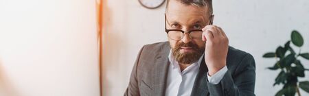 panoramic shot of handsome businessman in formal wear and glasses looking at camera の写真素材
