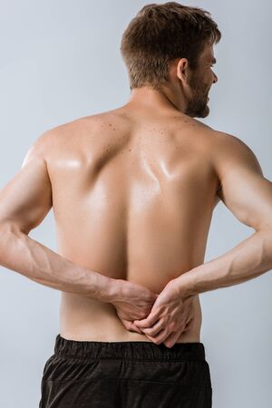back view of shirtless sportsman with lower back pain isolated on greyの写真素材