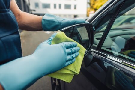cropped view of car cleaner wiping side mirror od car with rag