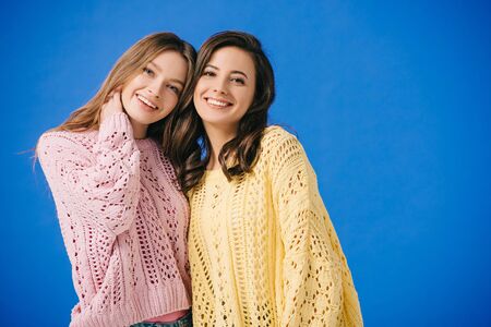 attractive and smiling women in sweaters looking at camera isolated on blueの写真素材