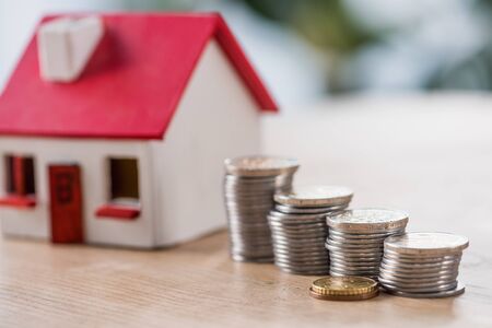 selective focus of stocked silver and golden coins near toy house on wooden tableの写真素材