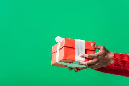 cropped view of African American man holding red gift box with white ribbon isolated on greenの写真素材