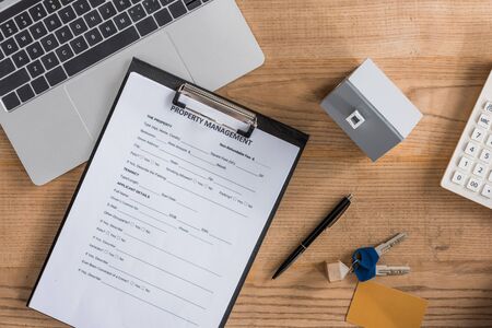 top view of clipboard with property management agreement, house model, laptop, keys and pen on wooden deskの写真素材