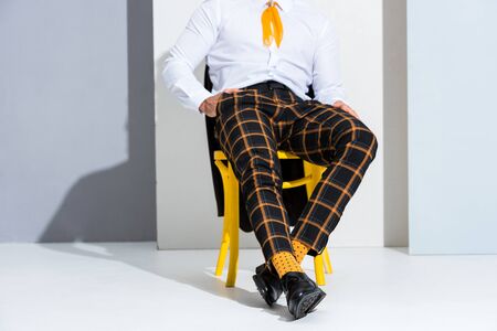 cropped view of man sitting with hand in pocket on white and greyの写真素材