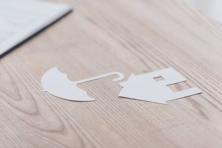 white paper cut house and umbrella on wooden desk in office
