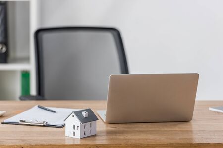 house model, laptop and clipboard with pen on wooden desk near office chairの写真素材