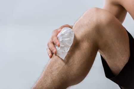 partial view of sportsman using ice for knee isolated on grey