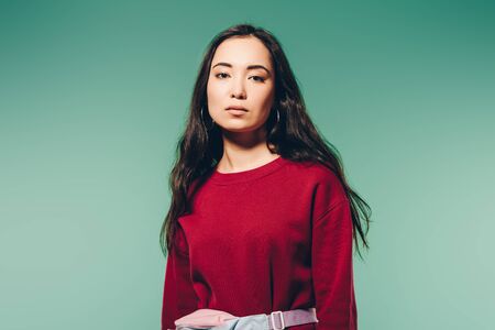 attractive asian woman in red sweater looking at camera isolated on green