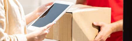 panoramic shot of delivery man holding package near woman with digital tablet 