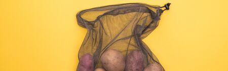 top view of potatoes in eco friendly black mesh bag isolated on yellow, panoramic shotの写真素材