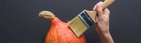 panoramic shot of woman holding paintbrush on pumpkin on black backgroundの写真素材