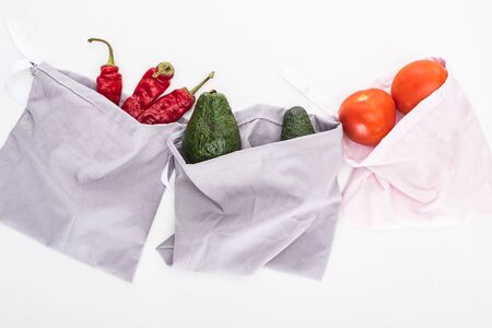 top view of fresh avocados, tomatoes and chili peppers in eco friendly bags isolated on whiteの写真素材