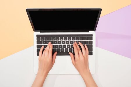 cropped view of woman using laptop on beige, violet and white backgroundの写真素材