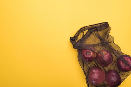 top view of apples in eco friendly black mesh bag isolated on yellowの写真素材