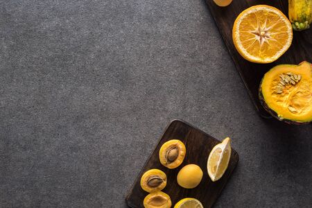 top view of yellow fruits and vegetables on wooden cutting boards on grey textured background with copy spaceの写真素材