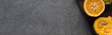top view of orange and pumpkin on wooden cutting boards on grey textured background, panoramic shot
