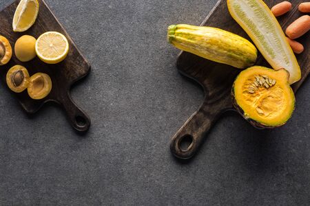top view of yellow fruits and vegetables on wooden cutting boards on grey textured background with copy spaceの写真素材