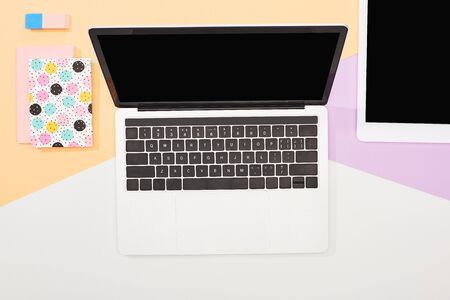top view of laptop with blank screen, digital tablet and office supplies on beige, violet and white backgroundの写真素材