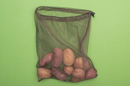 top view of fresh whole potatoes in eco friendly bag isolated on greenの写真素材