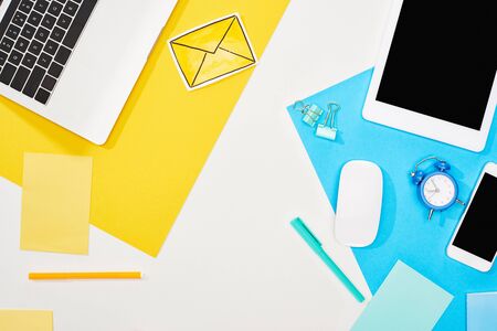 top view of laptop, smartphone, digital tablet with blank screen and computer mouse with office supplies on yellow, blue and white backgroundの写真素材
