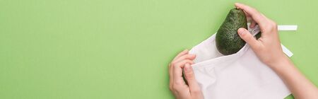 cropped view of woman putting avocado in eco friendly bag isolated on green, panoramic shotの写真素材