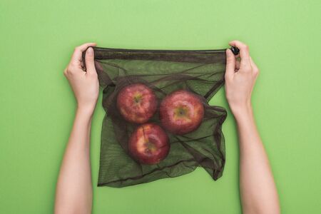 partial view of woman holding red ripe apples in eco friendly bag isolated on greenの写真素材