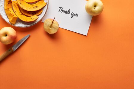 top view of pumpkin, apples, knife and thank you card on orange backgroundの写真素材