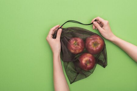 partial view of woman holding red ripe apples in eco friendly bag isolated on greenの写真素材