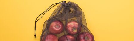 top view of red apples in eco friendly black mesh bag isolated on yellow, panoramic shotの写真素材