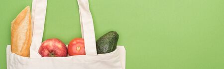 top view of tomato, avocado, apple and baguette in eco friendly bag isolated on green, panoramic...