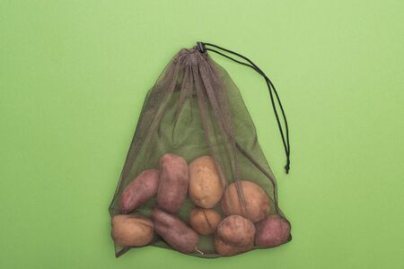 top view of fresh whole potatoes in eco friendly bag isolated on greenの写真素材