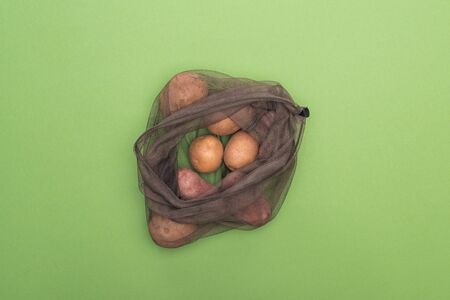 top view of fresh whole potatoes in eco friendly bag isolated on greenの写真素材