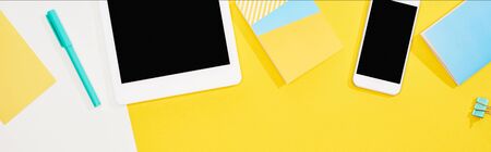 top view of digital tablet, smartphone with blank screen and office supplies on yellow and white...